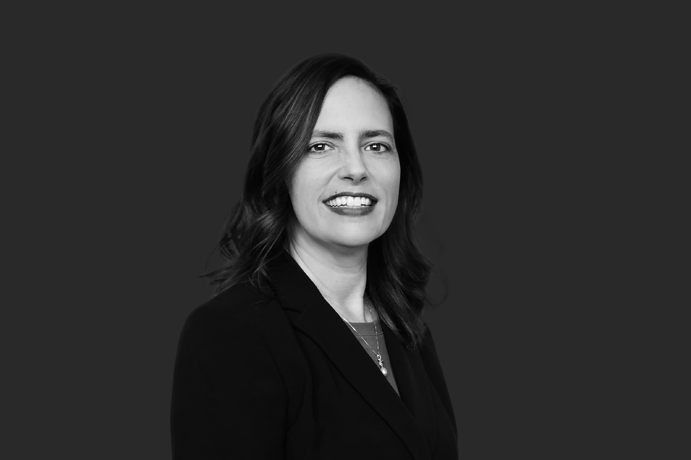Black and white headshot of a smiling woman with wavy hair wearing a professional blazer.