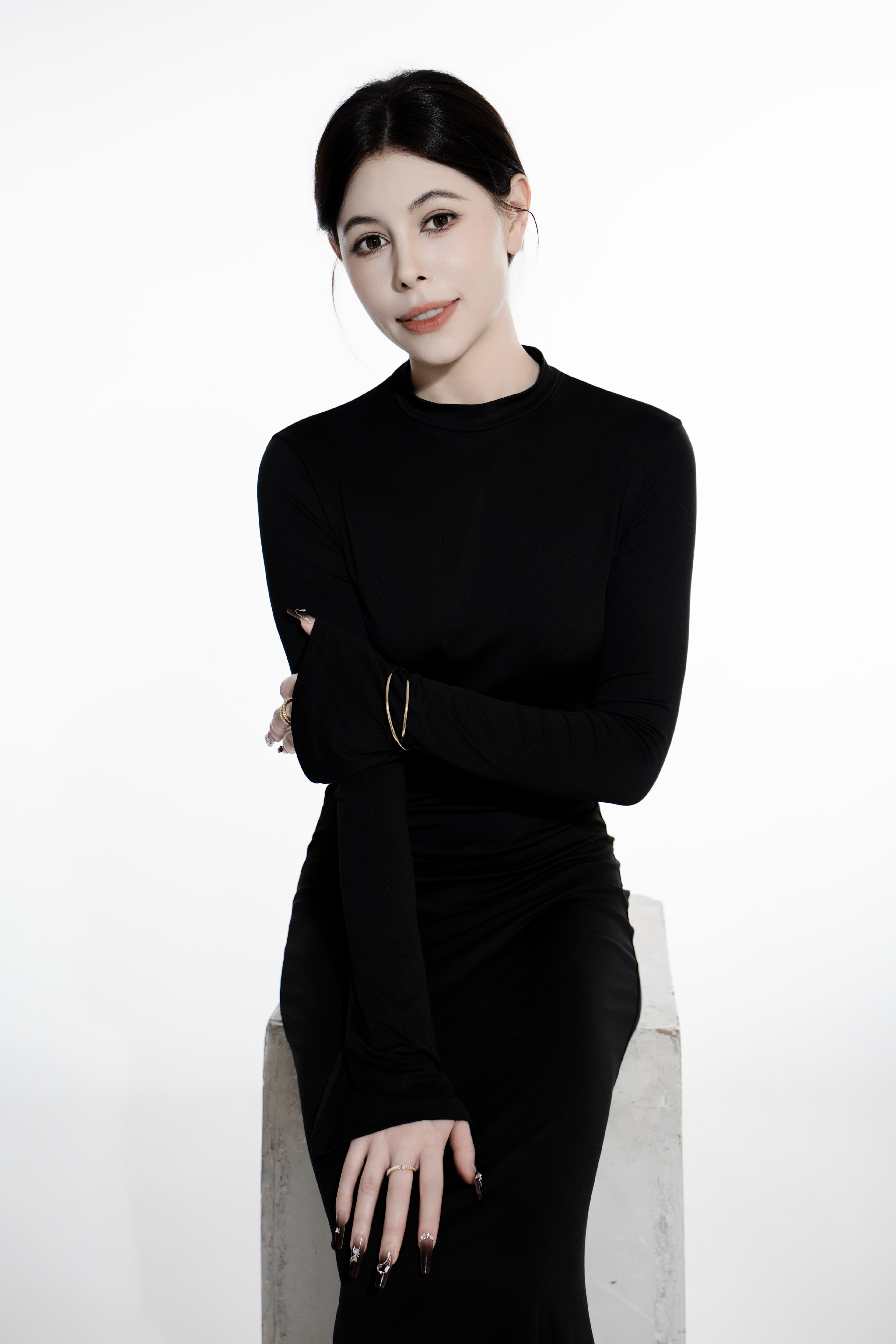 Woman with dark hair wearing a black long-sleeved dress sitting on a white block.