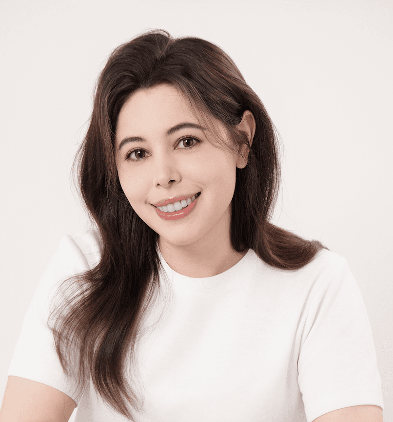 Portrait of a smiling woman with long brown hair wearing a simple white t-shirt.
