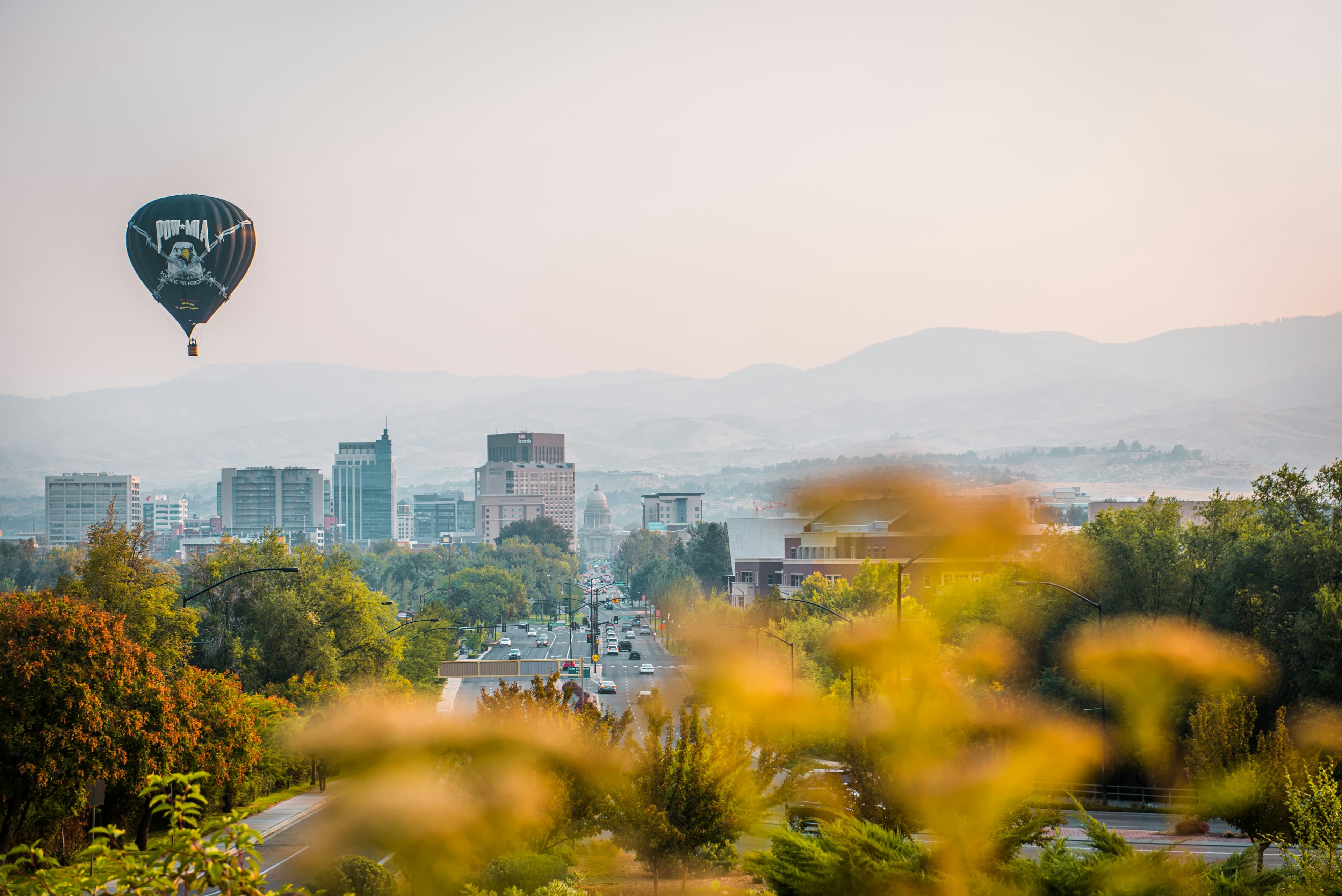 Black POW-MIA hot air balloon floating over a city skyline with hazy mountains beyond.